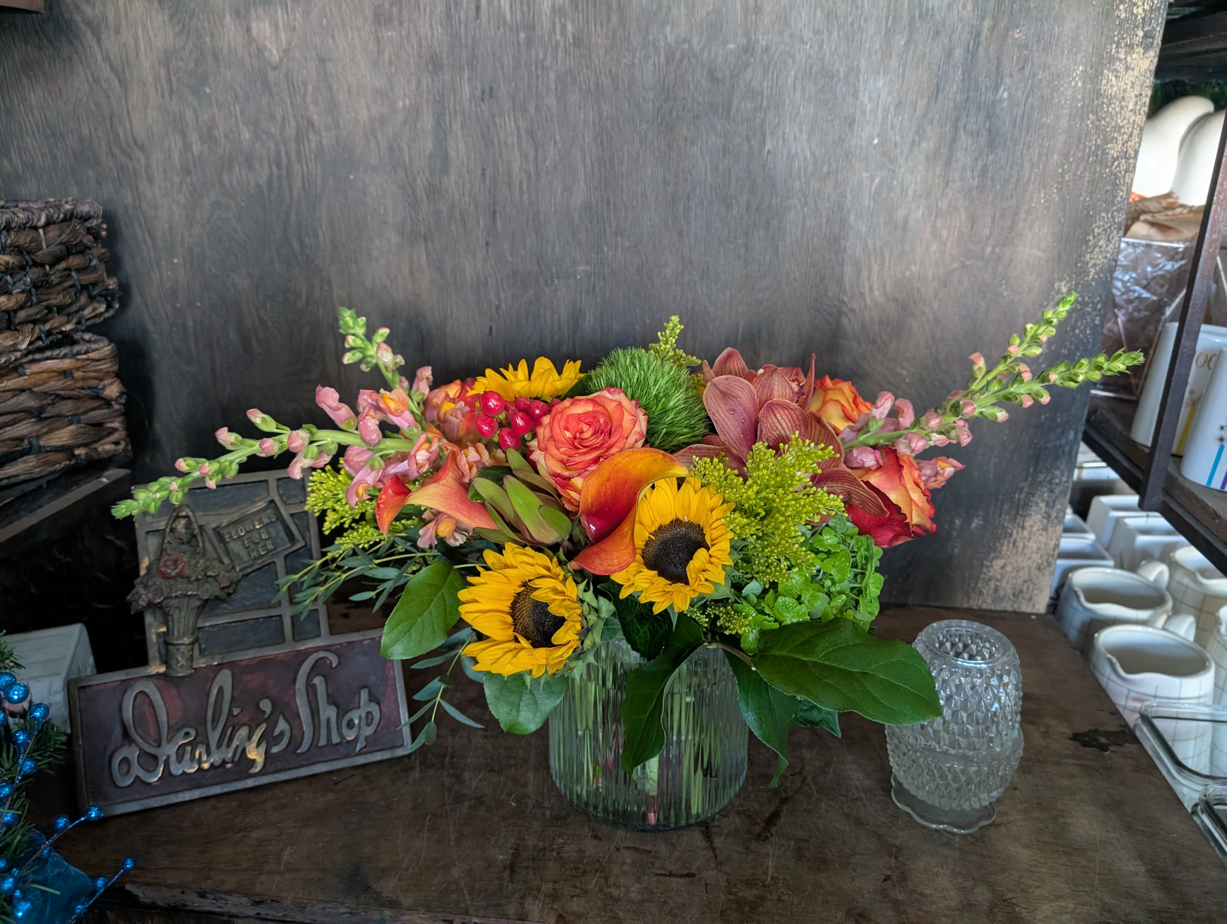 Mixed bouquet of sunflowers, roses, and orchids in a glass vase