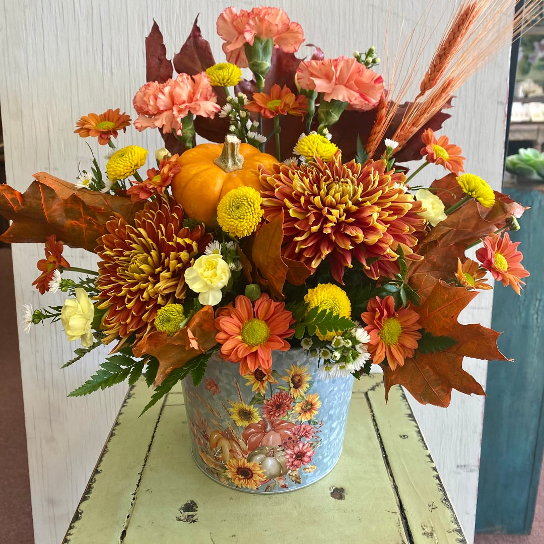 Autumn floral arrangement with orange and yellow blooms in a decorative tin bucket