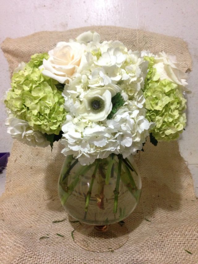 White and green floral arrangement in a round glass vase