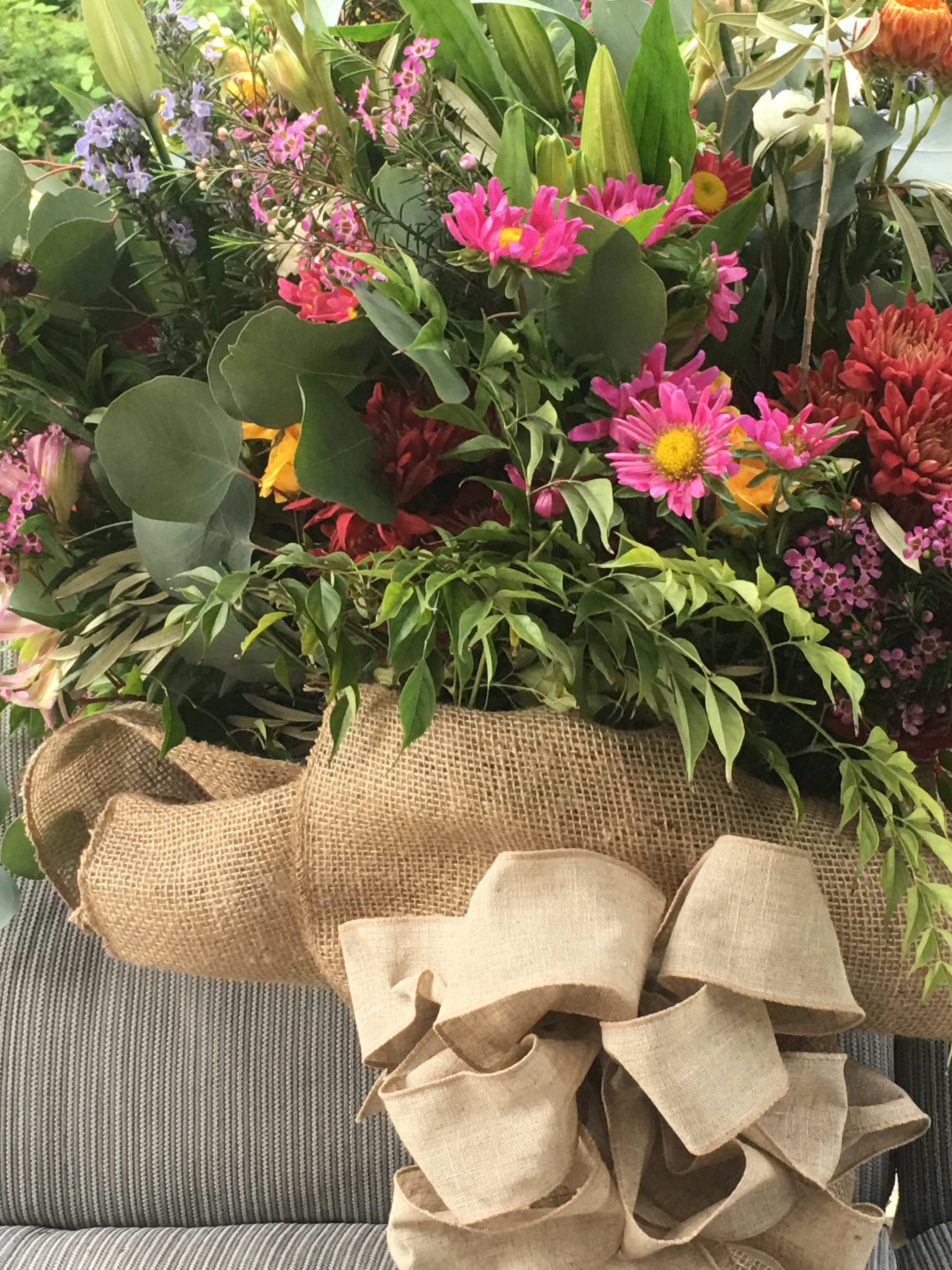 Mixed bouquet with pink and red flowers in burlap wrapping and a large beige bow