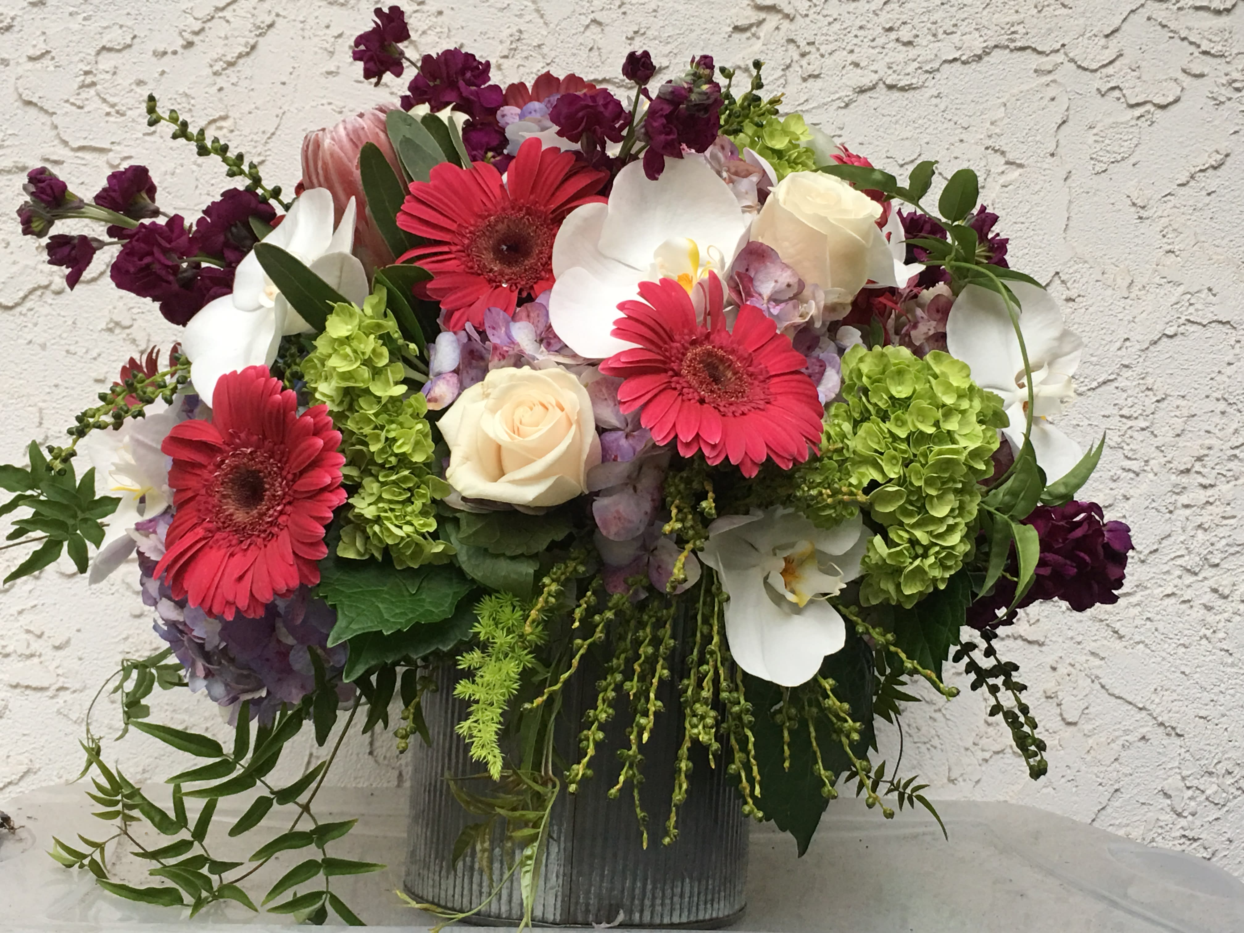 Mixed bouquet with pink gerbera daisies, white orchids, and cream roses in a ribbed vase