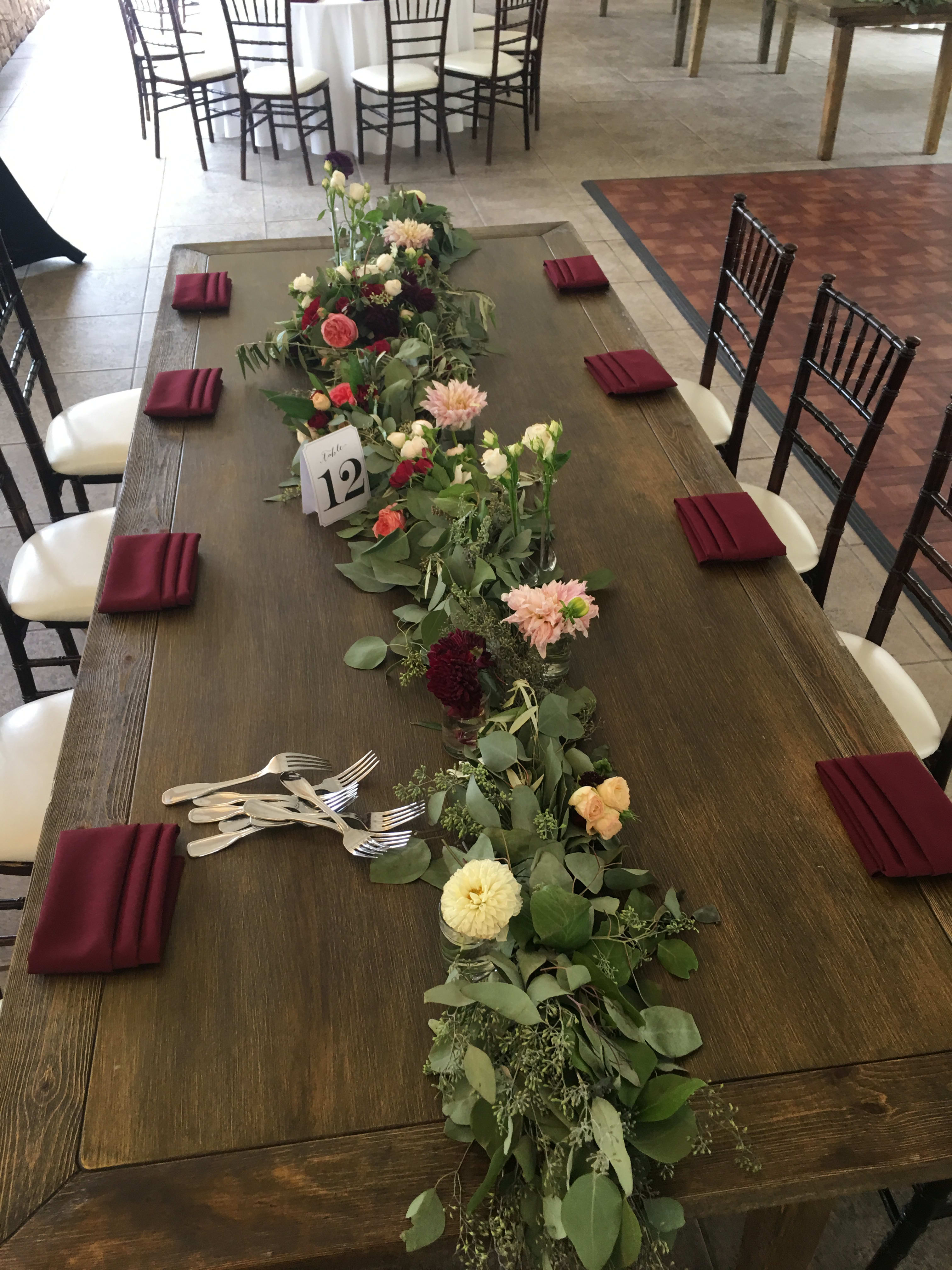 Long floral garland centerpiece on a dining table with small glass vases