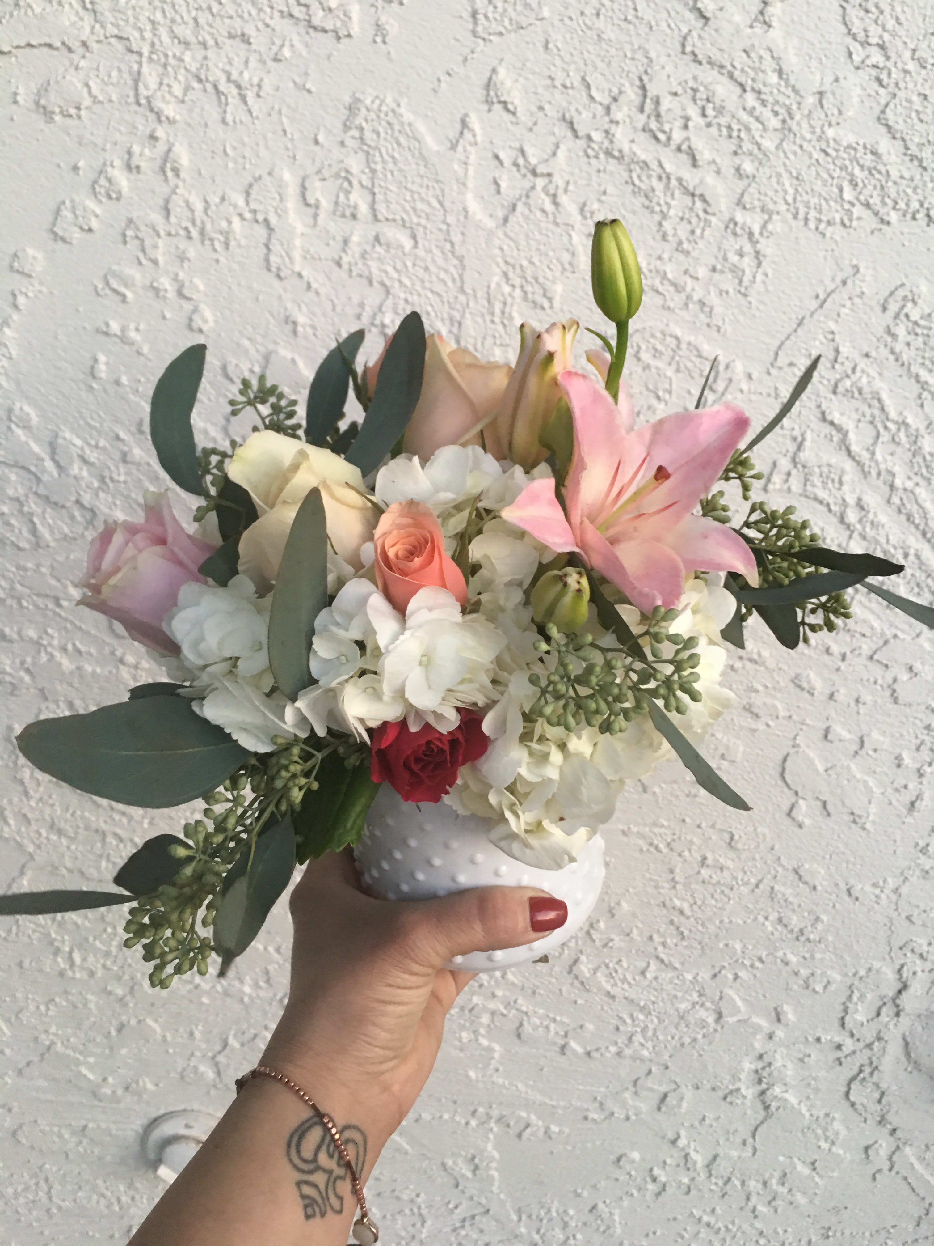 Handheld bouquet of pink lilies, roses, and white hydrangeas in a white vase
