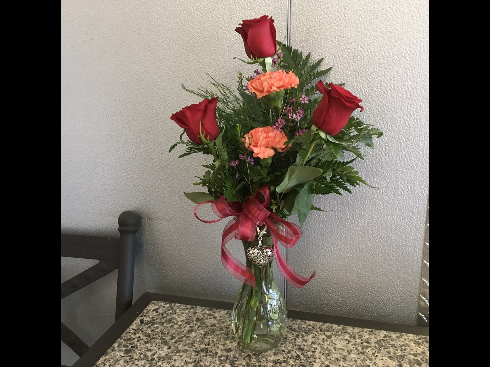 Red roses and orange carnations in a glass vase with a pink ribbon