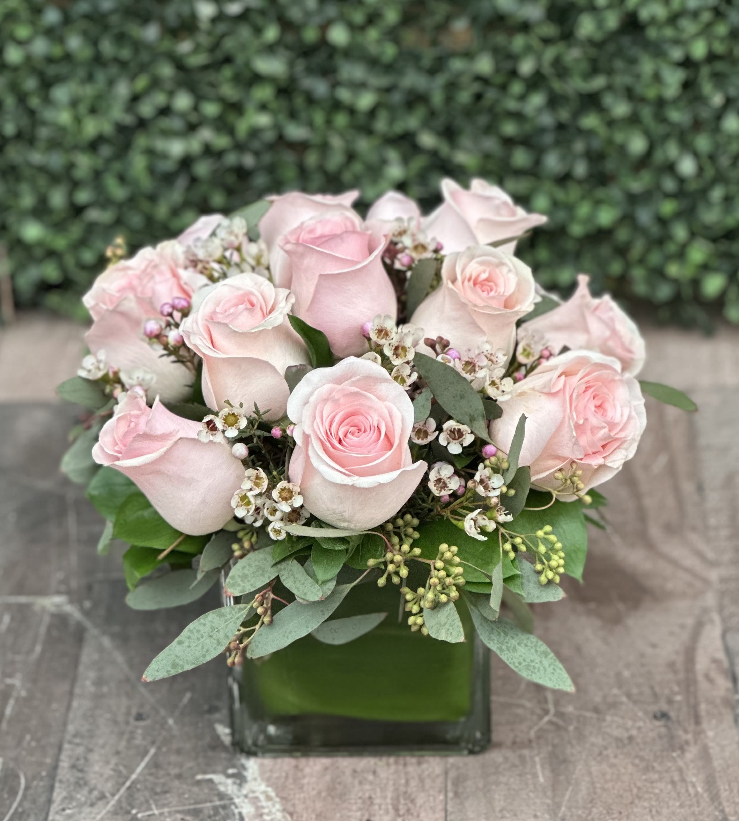 Pink roses arranged in a square glass vase with small white filler flowers