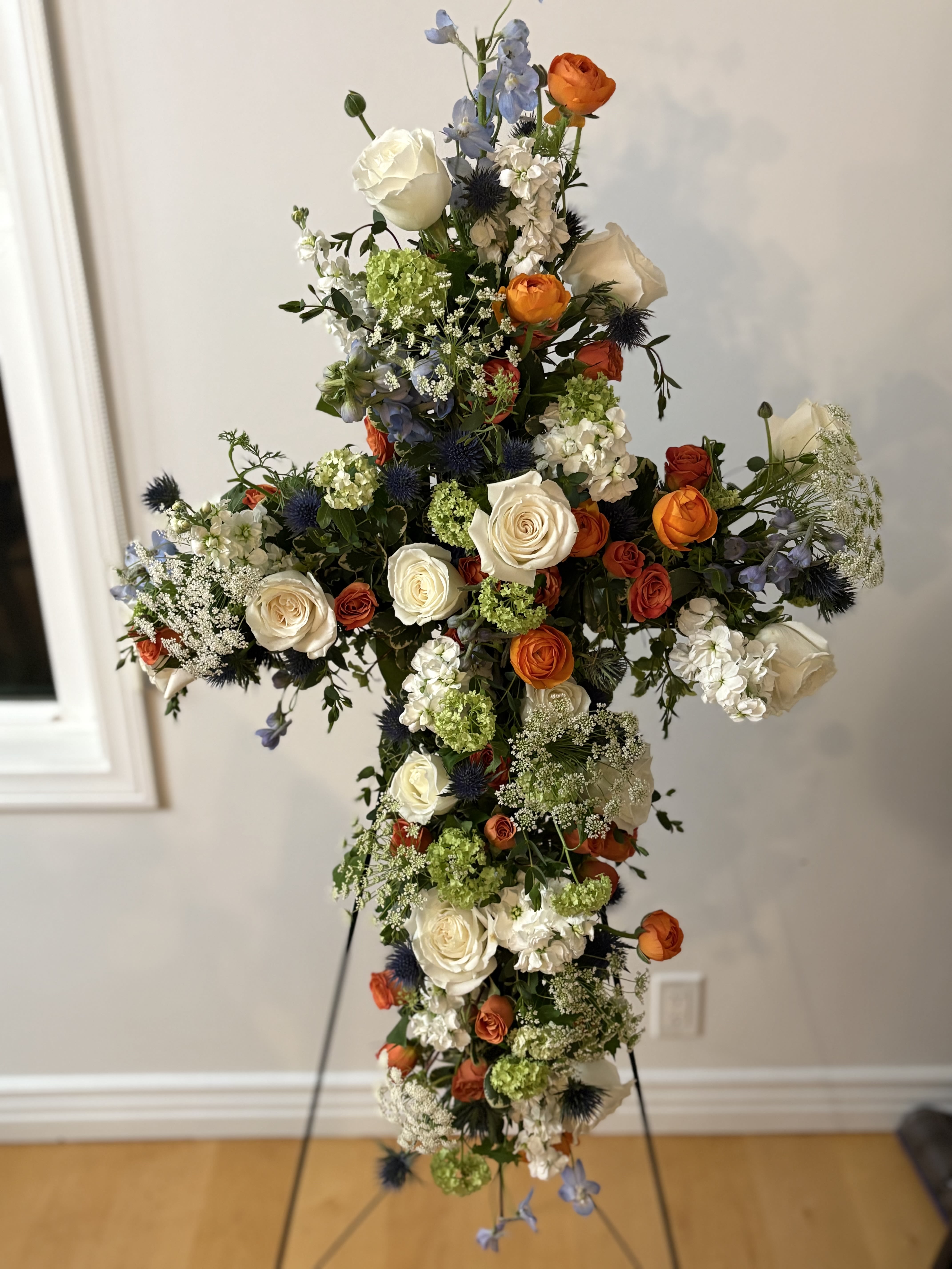 Tall floral cross with white, orange, blue, and green flowers