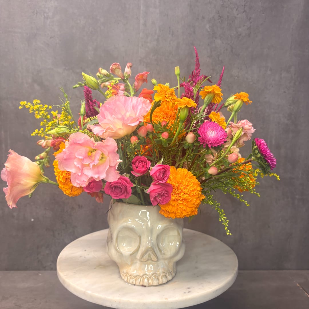 Mixed pink, orange, and yellow flowers in a skull-shaped vase