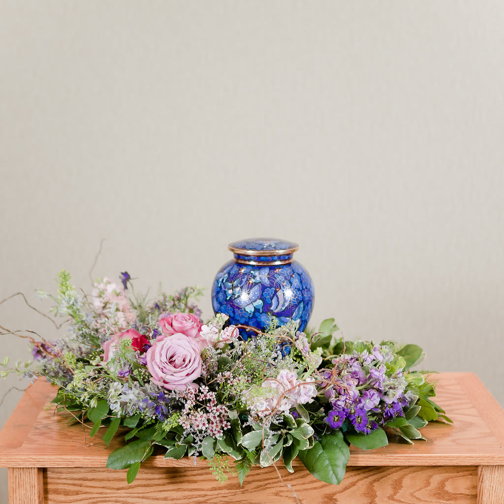 Low floral arrangement with pink and purple roses around a blue urn