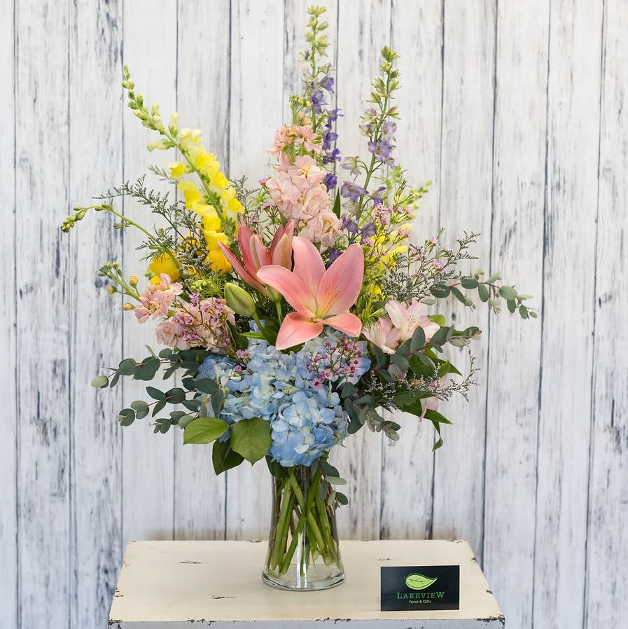 Mixed bouquet with pink lilies, blue hydrangea, and tall yellow and purple blooms in a glass vase