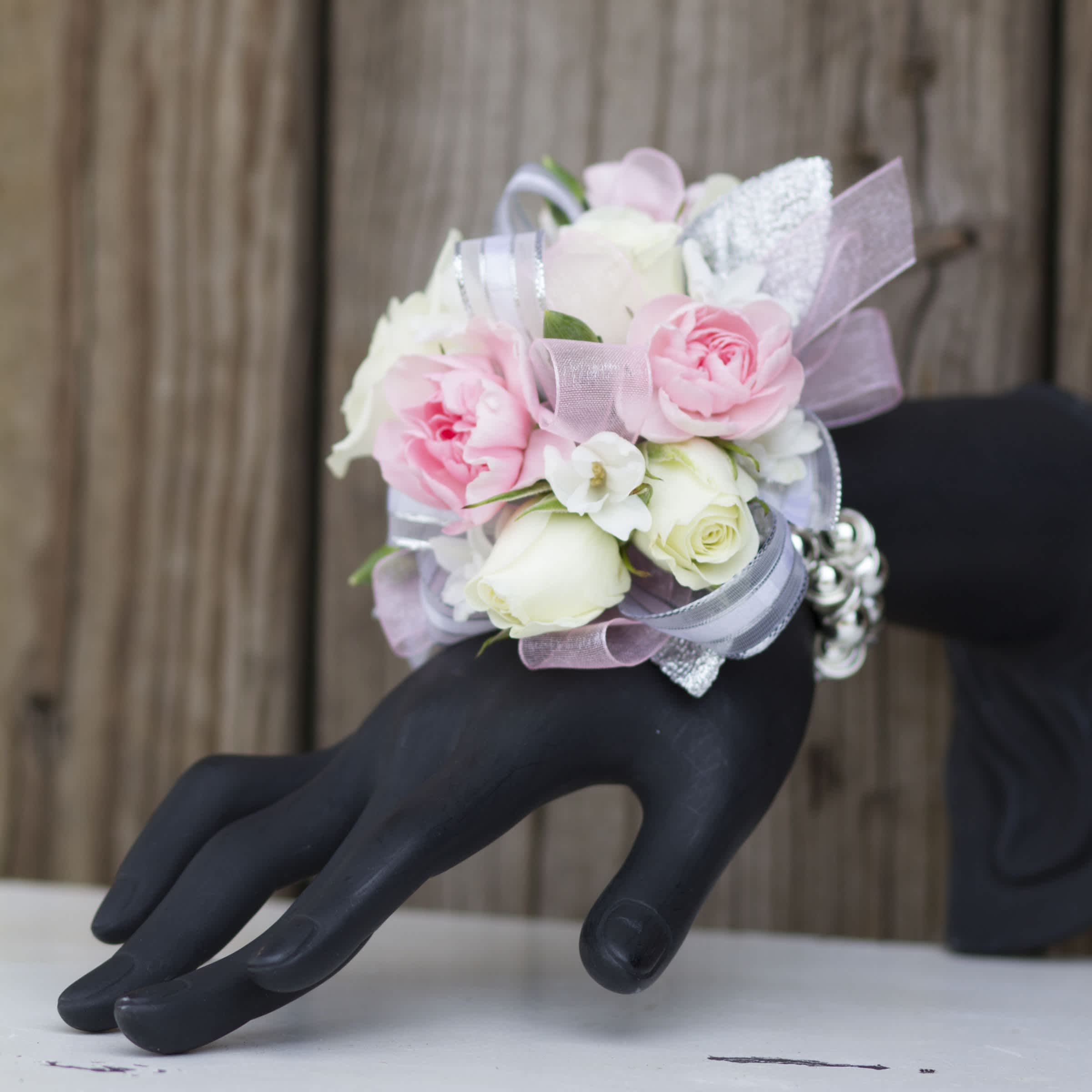 Pink and white rose wrist corsage with ribbons on a black mannequin hand