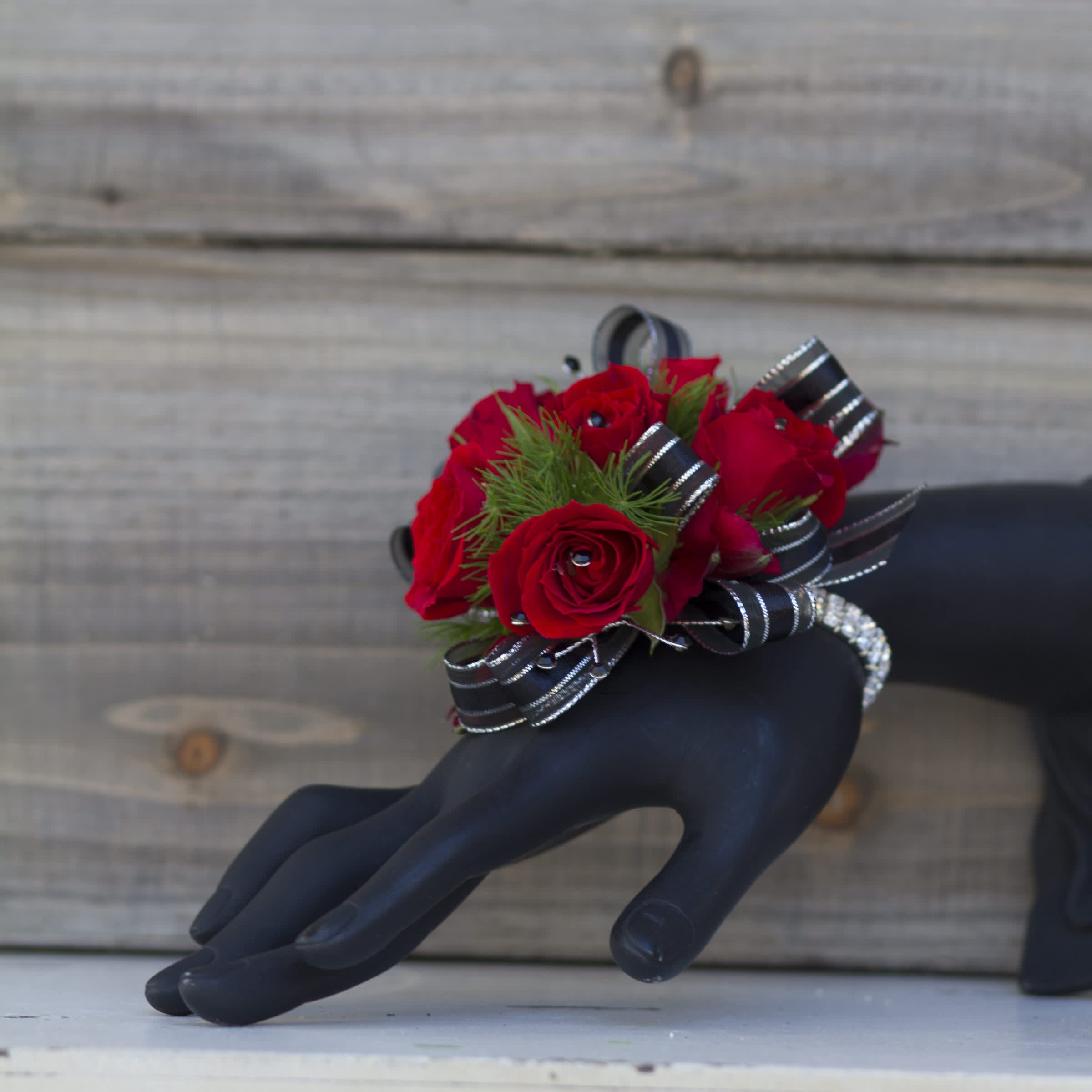 Red rose wrist corsage with black striped ribbon on a black mannequin hand