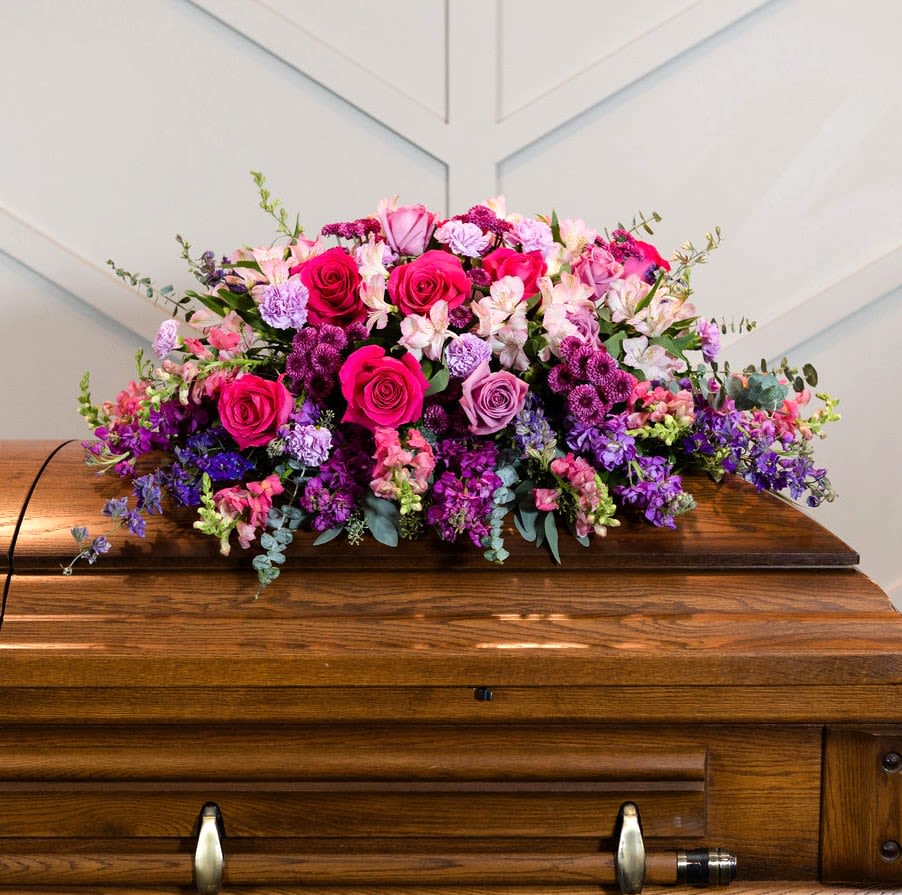 Large pink and purple floral arrangement on a wooden casket