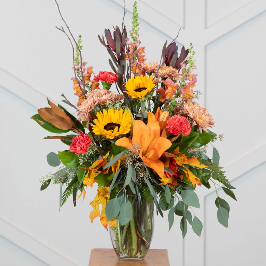 Autumn bouquet with sunflowers, lilies, and carnations in a glass vase