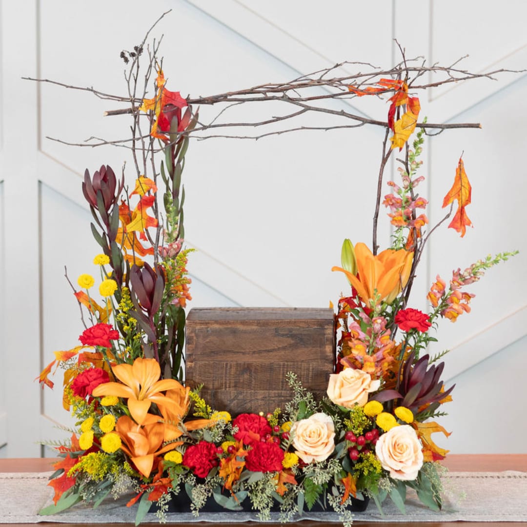 Autumn floral arrangement with roses, lilies, and branches around a wooden box