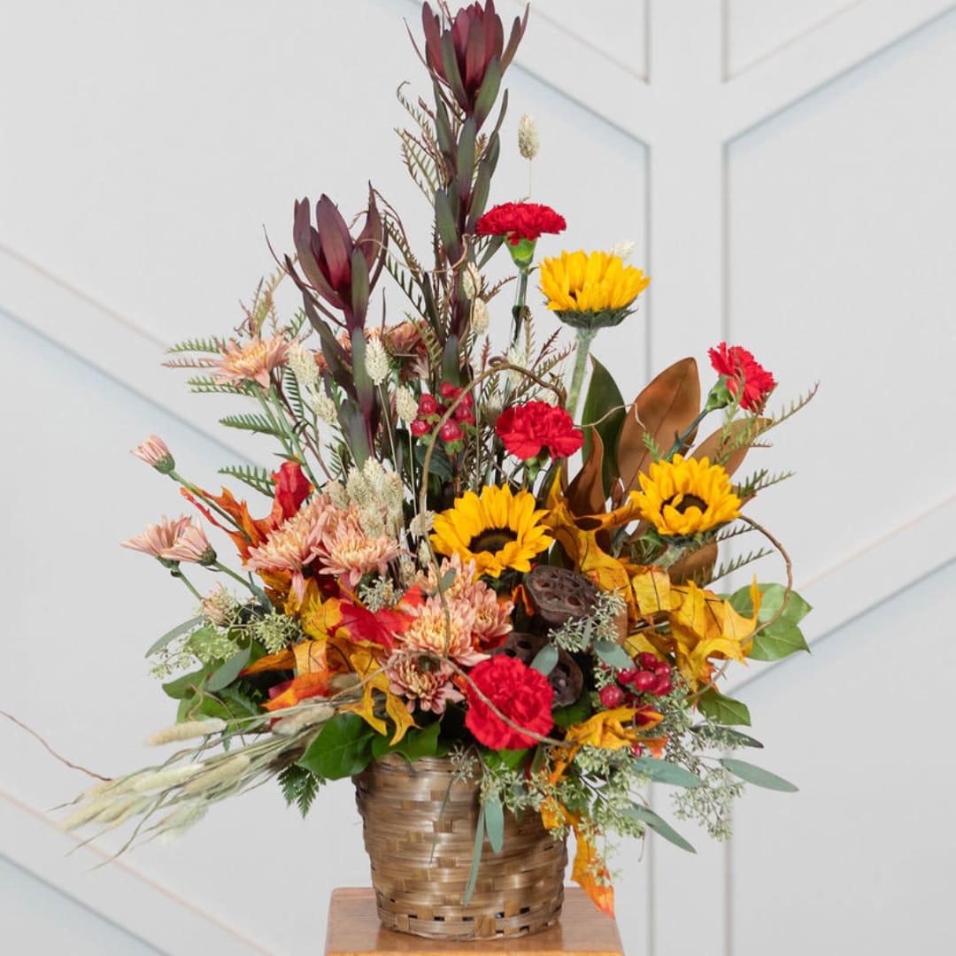 Autumn floral arrangement with sunflowers and red carnations in a woven basket