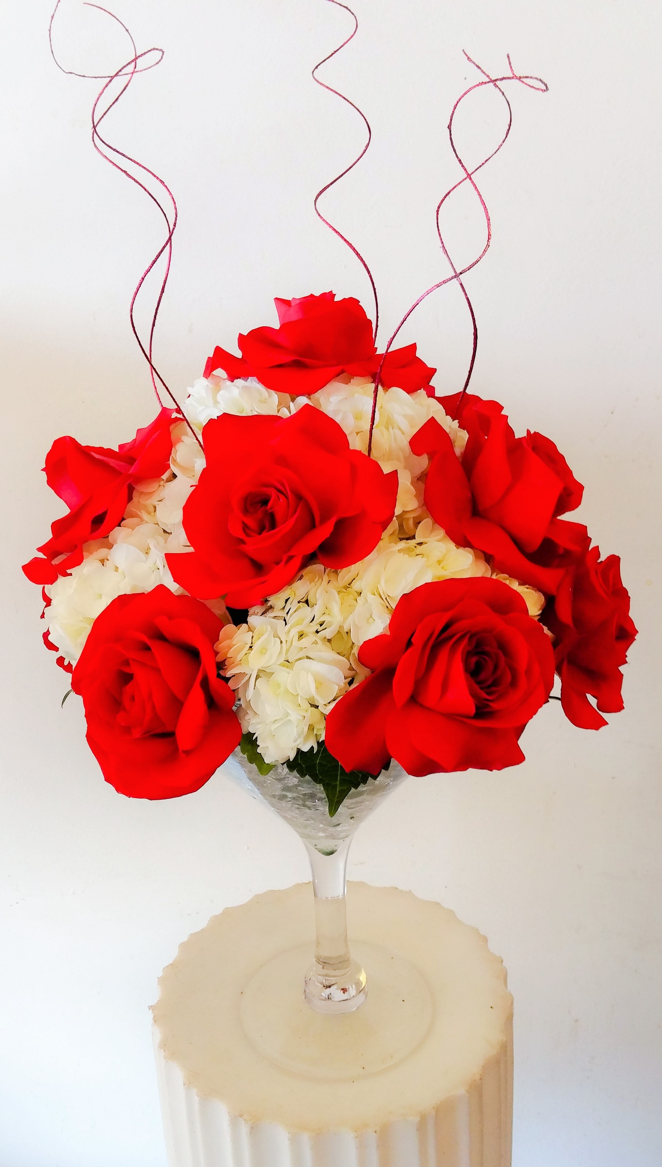 Red roses and white hydrangeas in a clear stemmed vase