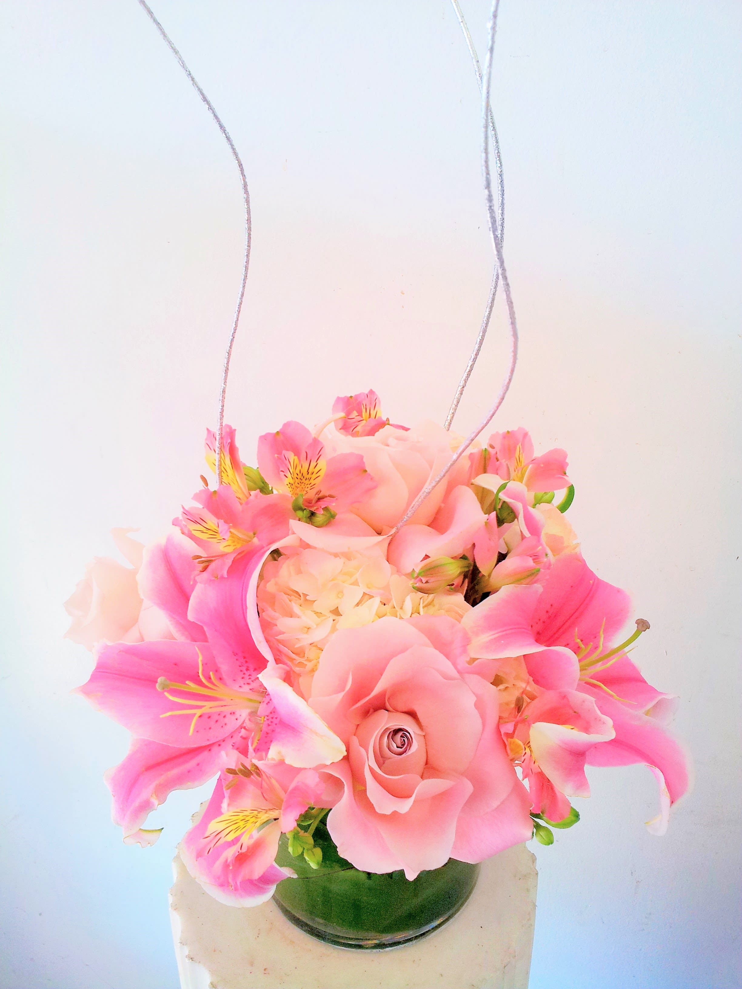 Pink floral arrangement in a glass vase with hanging silver cords