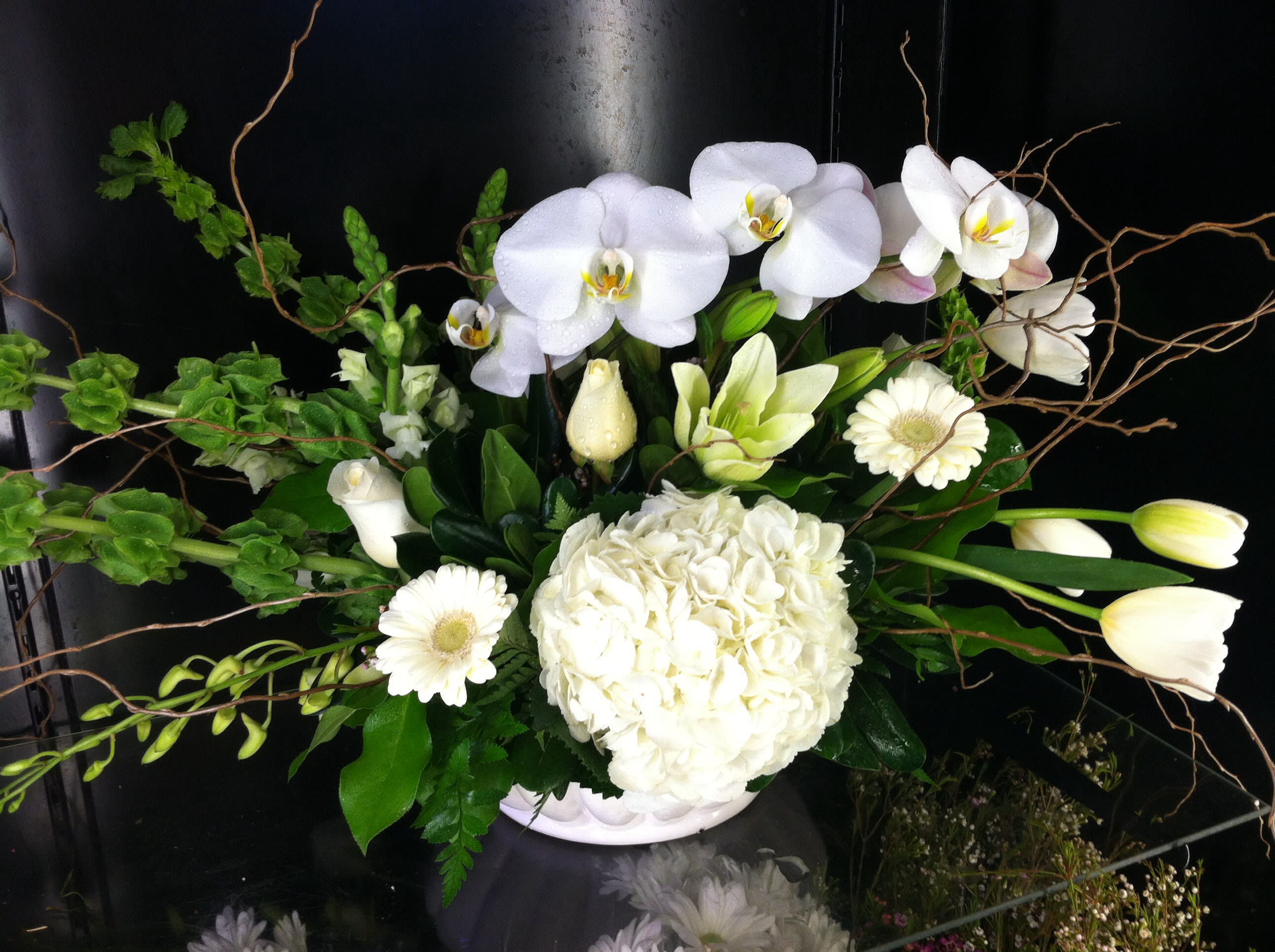 Low white arrangement with orchids, hydrangea, tulips, roses, lilies, and gerberas in a white bowl.