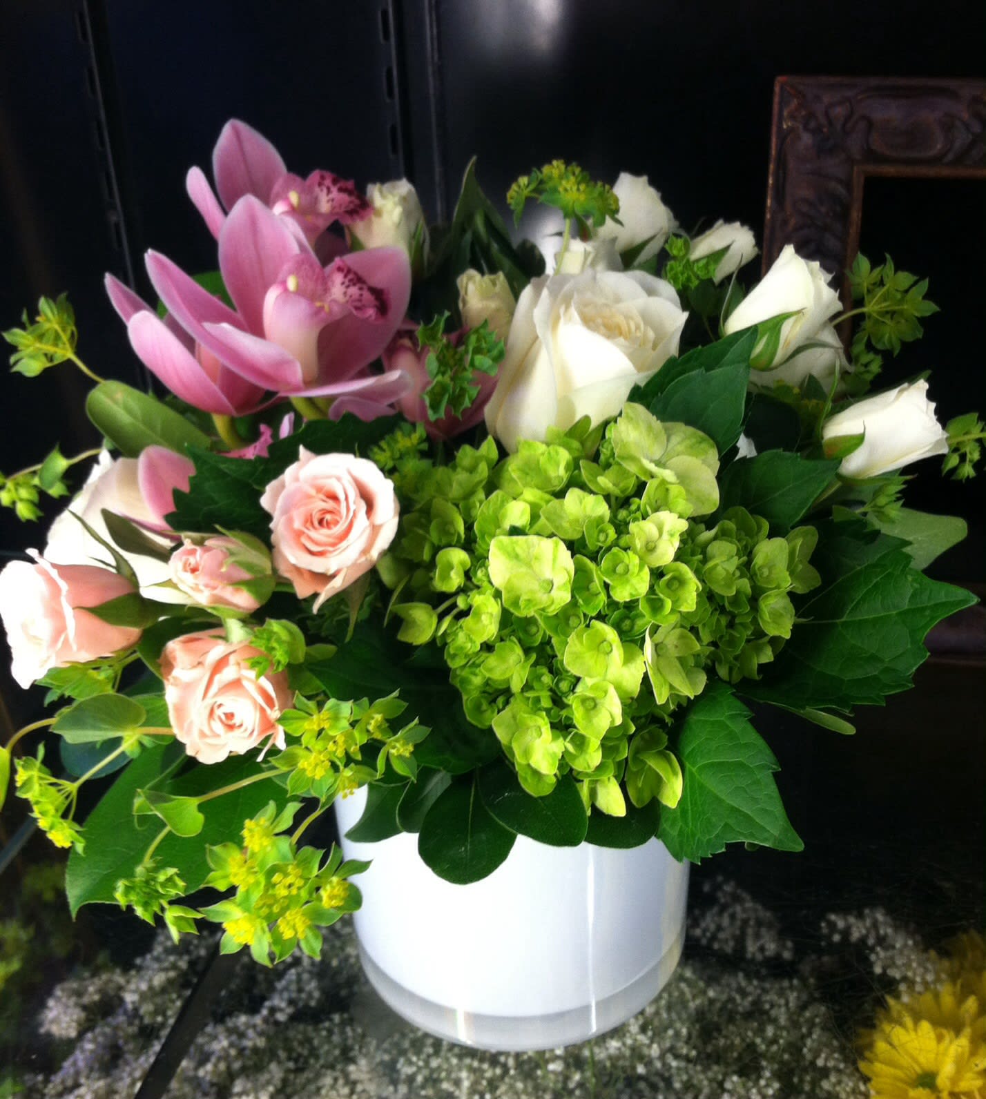 White vase arrangement with green hydrangea, white roses, pink orchids and spray roses.