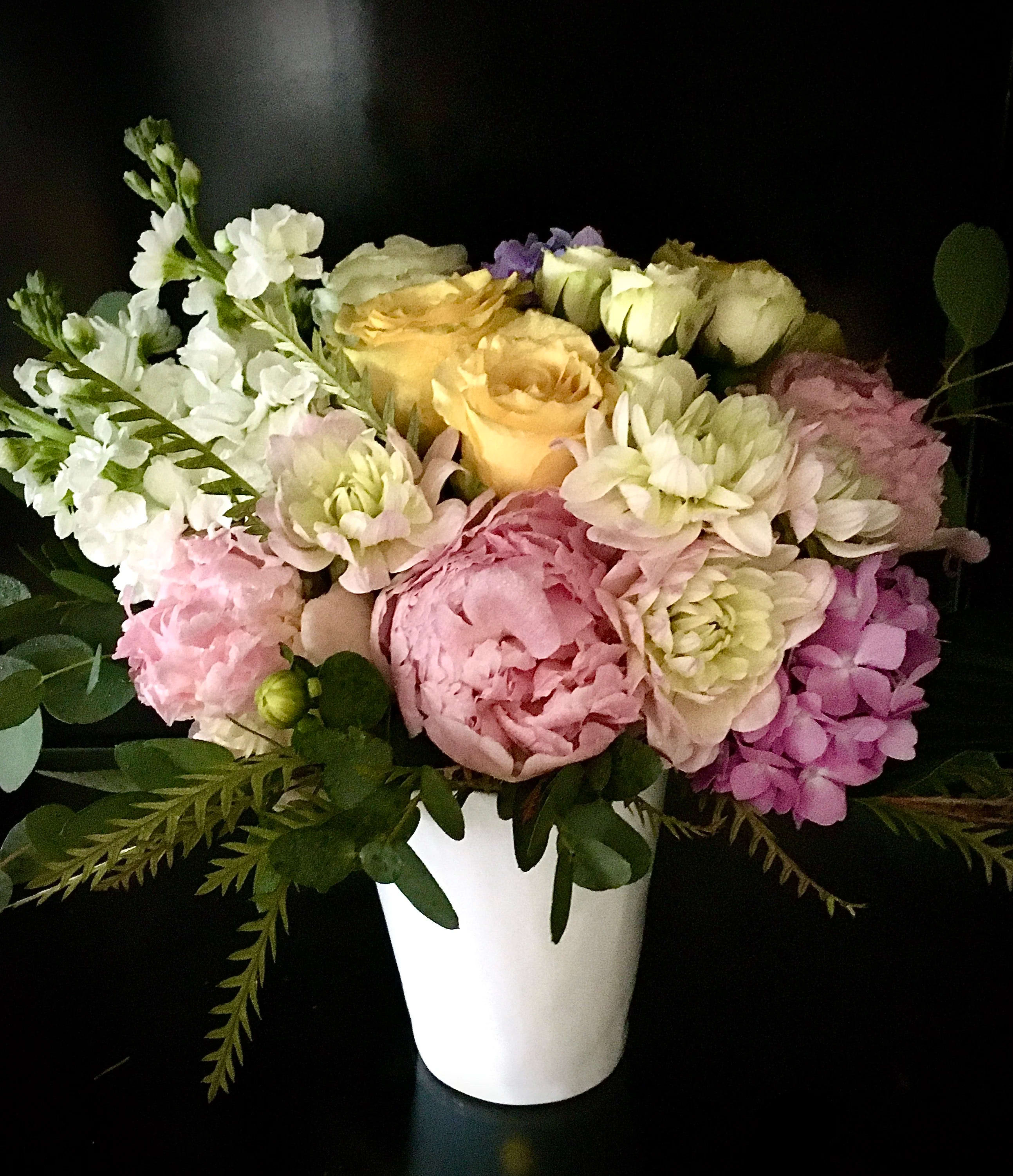 Pastel arrangement of pink peonies, yellow roses and white flowers in a white vase