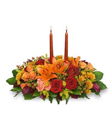 Low centerpiece of orange lilies, red and peach roses with two tall orange taper candles