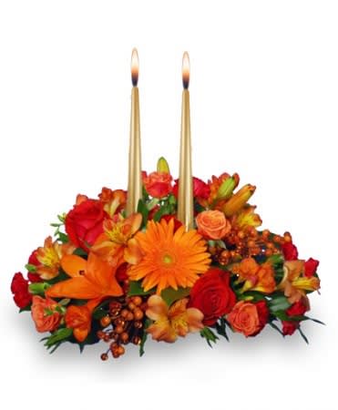 Low centerpiece of orange and red flowers with two tall gold taper candles in the center