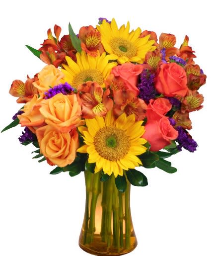 Bright arrangement of yellow sunflowers, orange roses, and purple accents in an amber glass vase