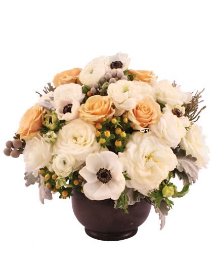 Low arrangement of white ranunculus and anemones with peach roses in a dark round bowl vase