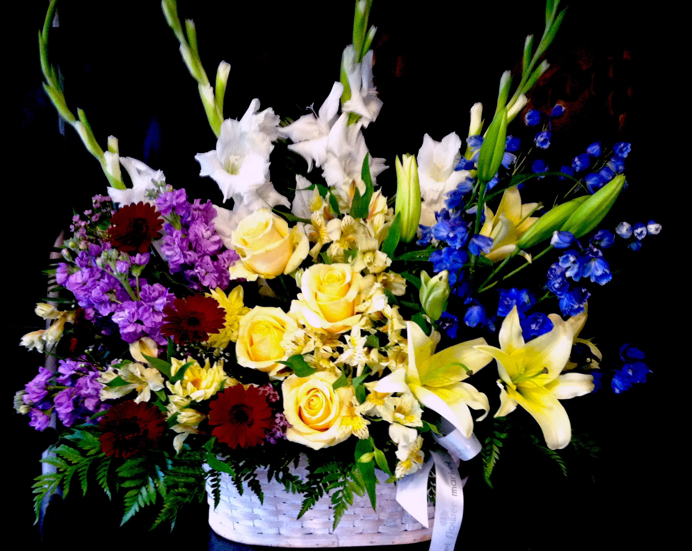 Tall mixed basket arrangement with yellow roses, lilies, white gladiolus, and blue delphinium.
