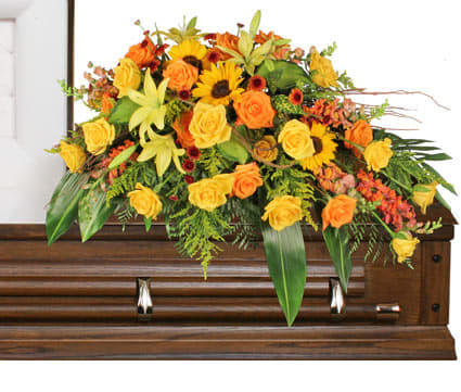 Yellow and orange casket spray of roses, lilies, and sunflowers on a wooden casket.