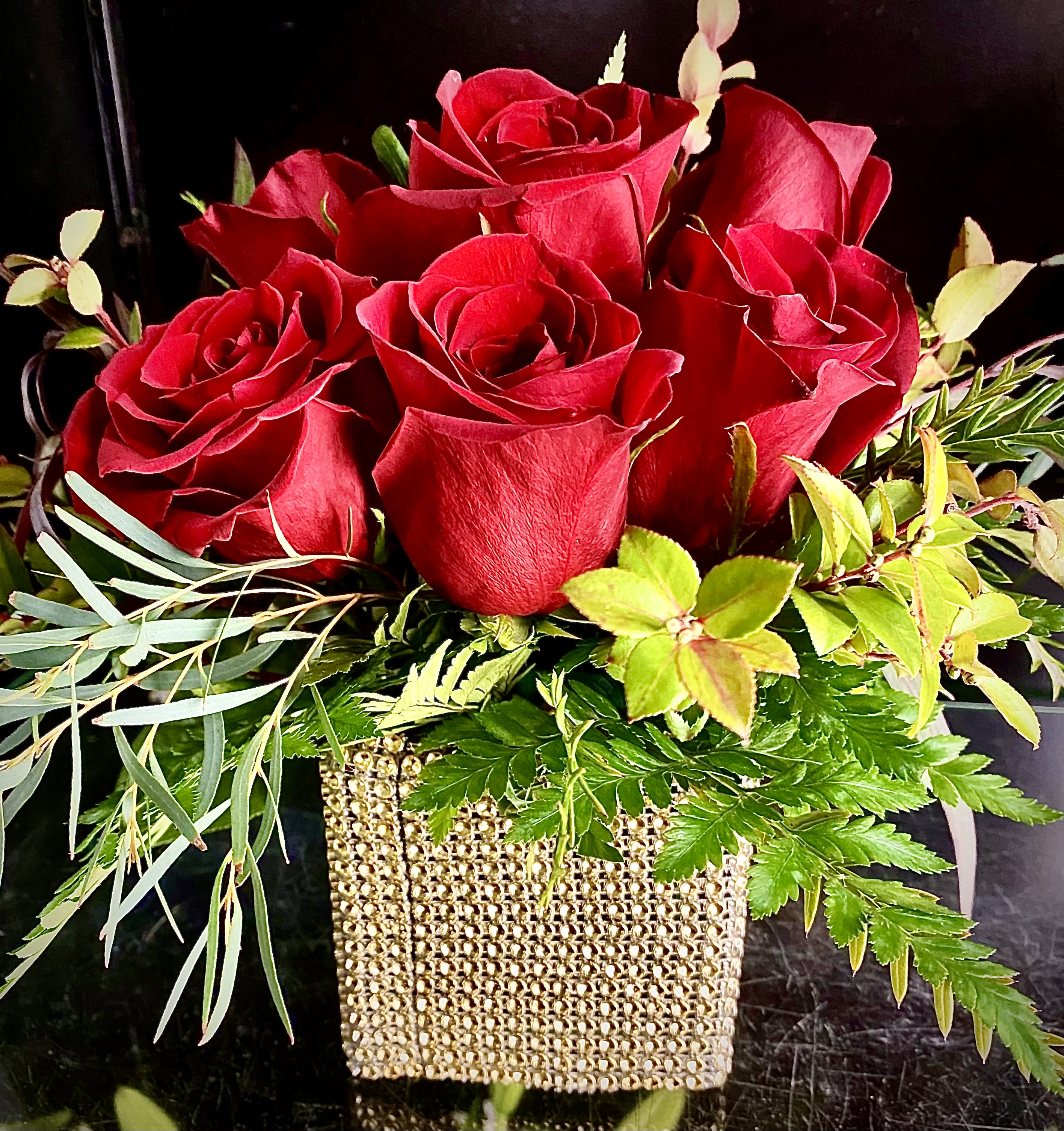 Low arrangement of red roses with foliage in a gold beaded cube vase