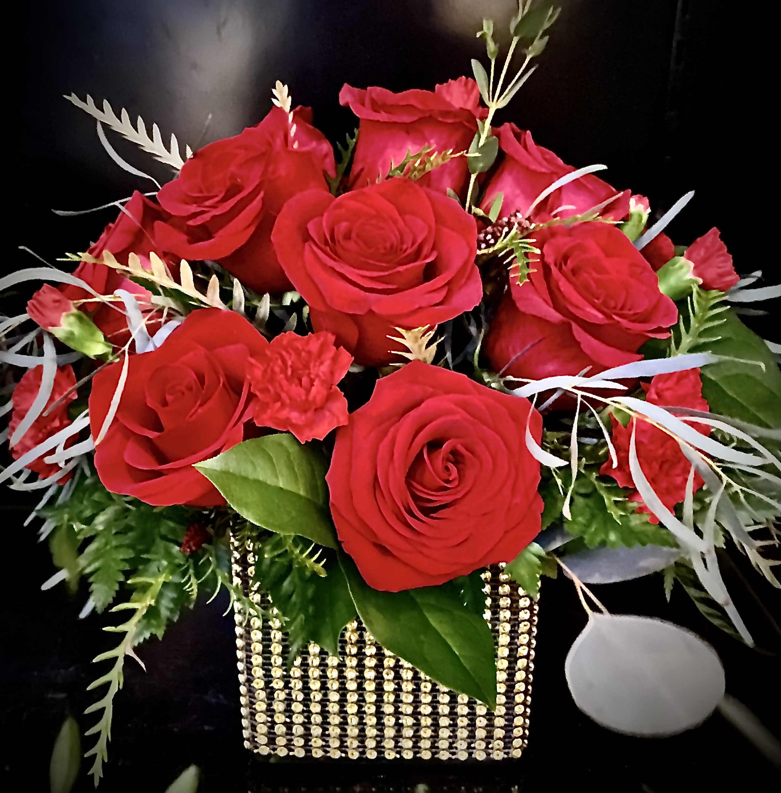Arrangement of red roses and small red flowers in a gold beaded cube vase