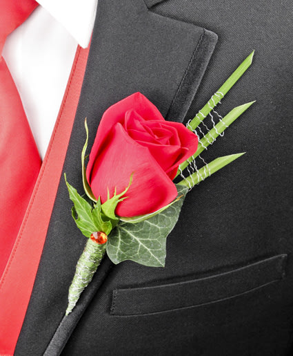 Single red rose boutonniere with decorative green blades on a black suit with red vest.