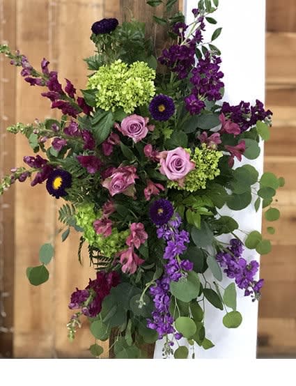 Asymmetrical purple and pink flower spray with green hydrangeas cascading from a wooden post.