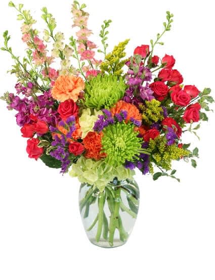 Tall mixed bouquet of bright roses, carnations, mums, and snapdragons in a clear glass vase