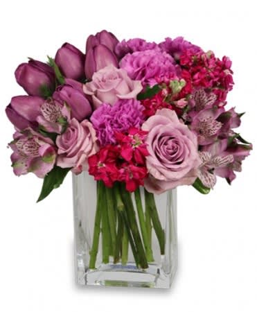 Compact arrangement of pink and purple roses, tulips, and mixed blooms in a clear glass vase