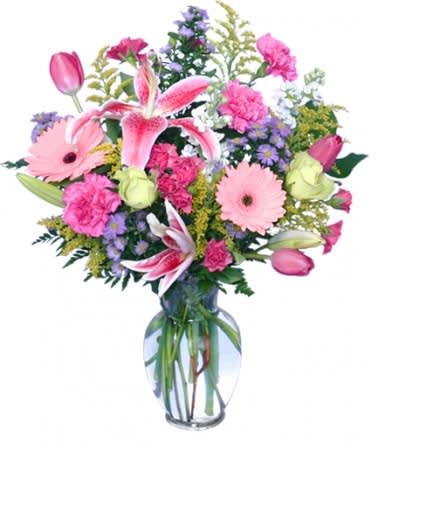 Mixed bouquet of pink lilies, tulips, carnations, and daisies in a clear glass vase