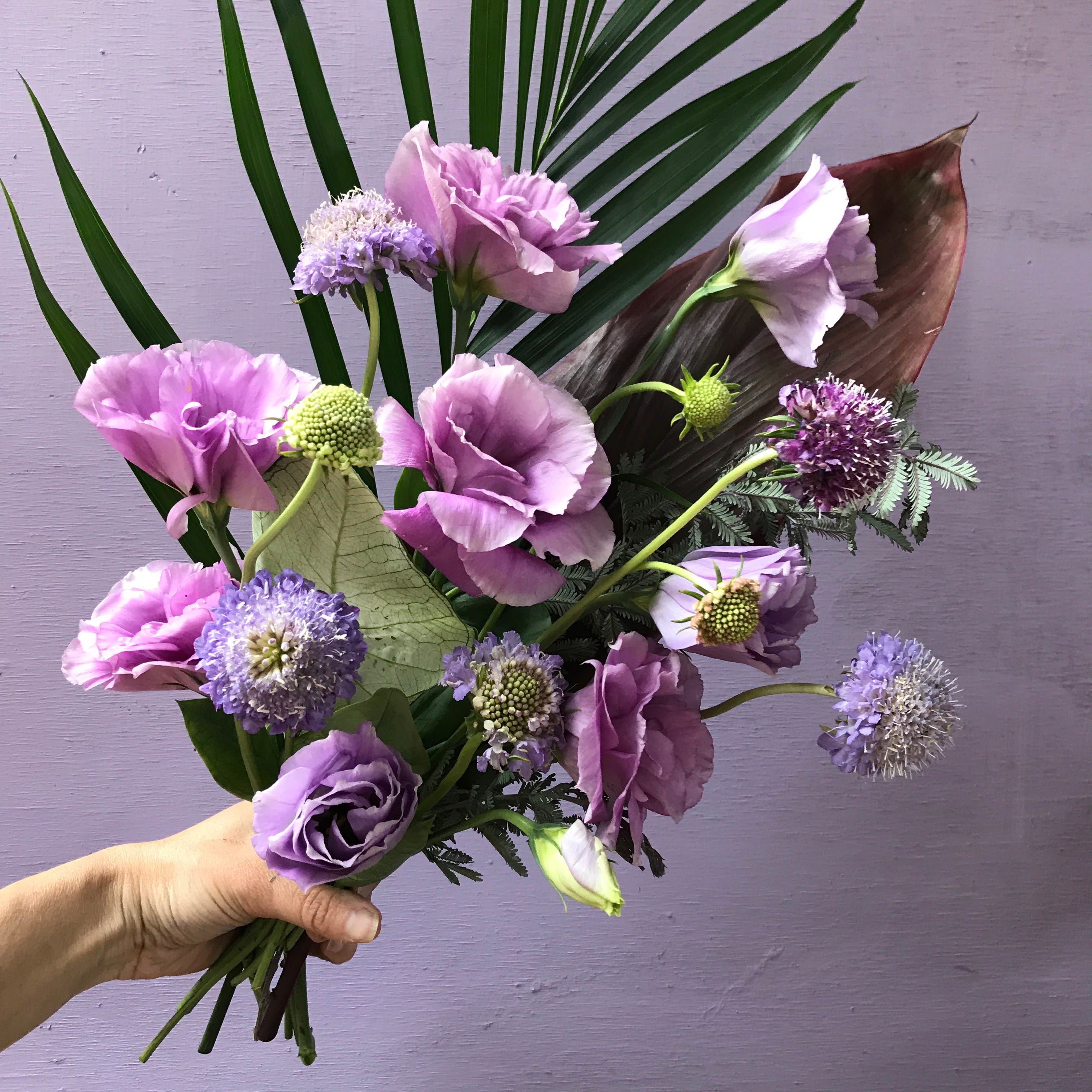 Handheld bouquet of lavender flowers with palm fronds