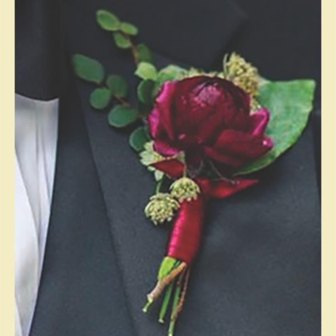 Red boutonniere with greenery pinned to a dark suit lapel