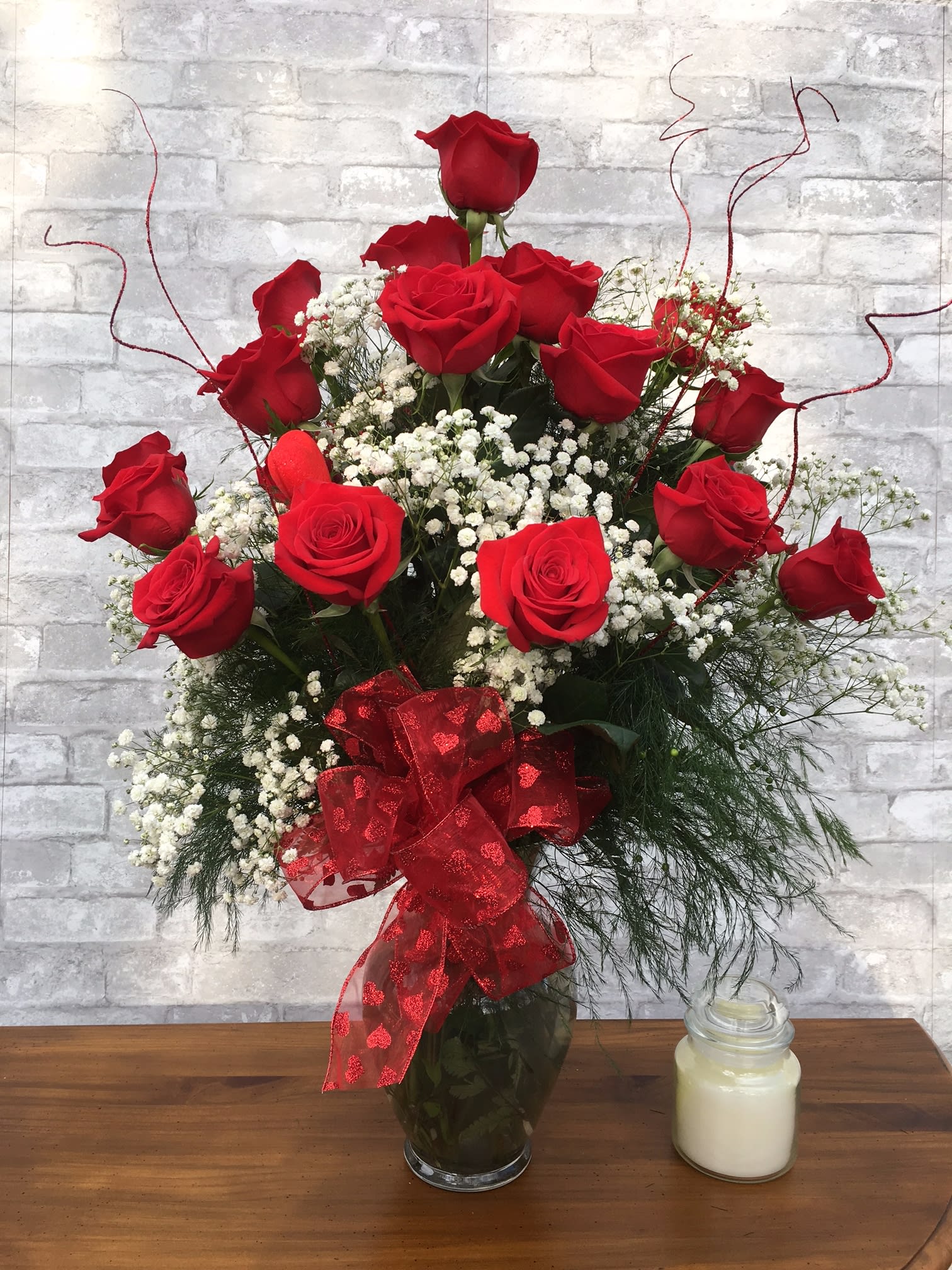 Red roses arranged in a glass vase with baby's breath and a red ribbon