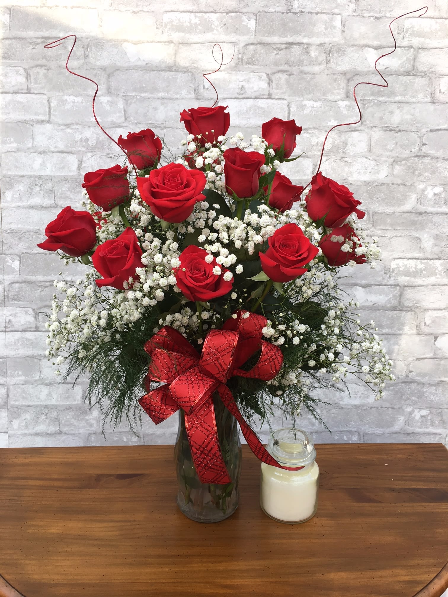 Red roses in a glass vase with baby's breath and a red ribbon