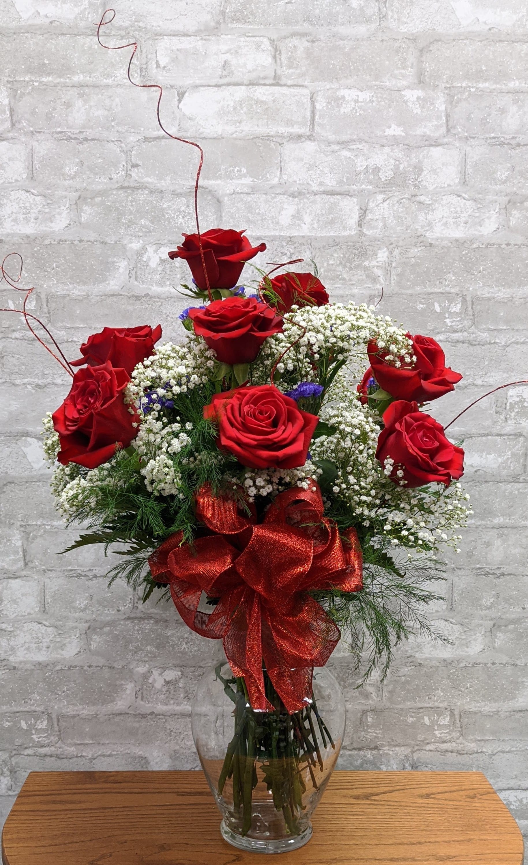Red roses arranged in a clear glass vase with a red ribbon bow