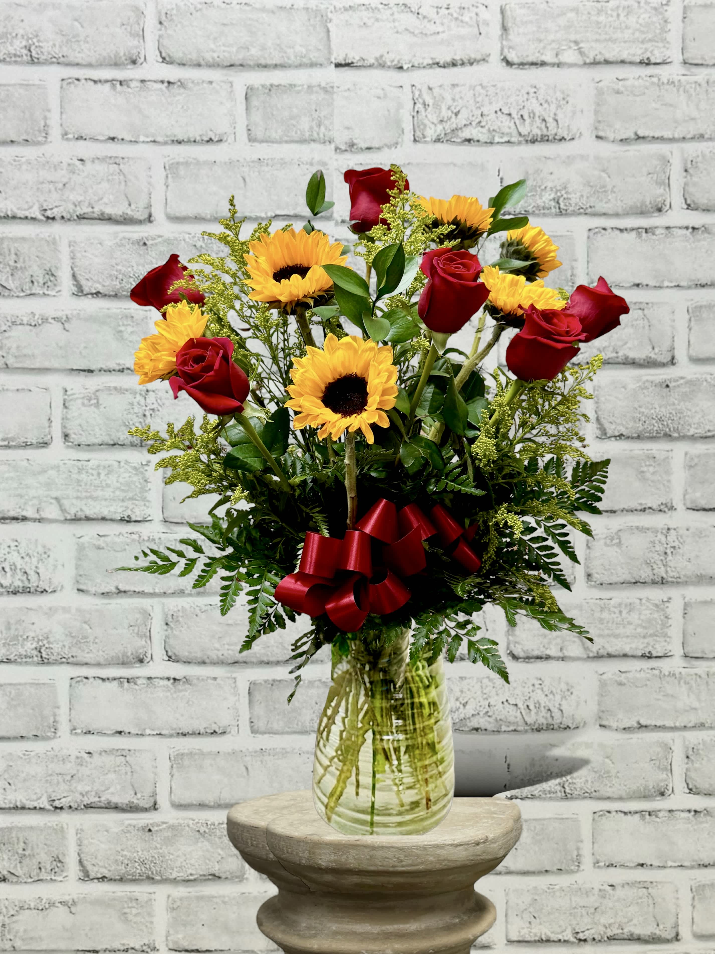 Red roses and yellow sunflowers in a glass vase with a red ribbon