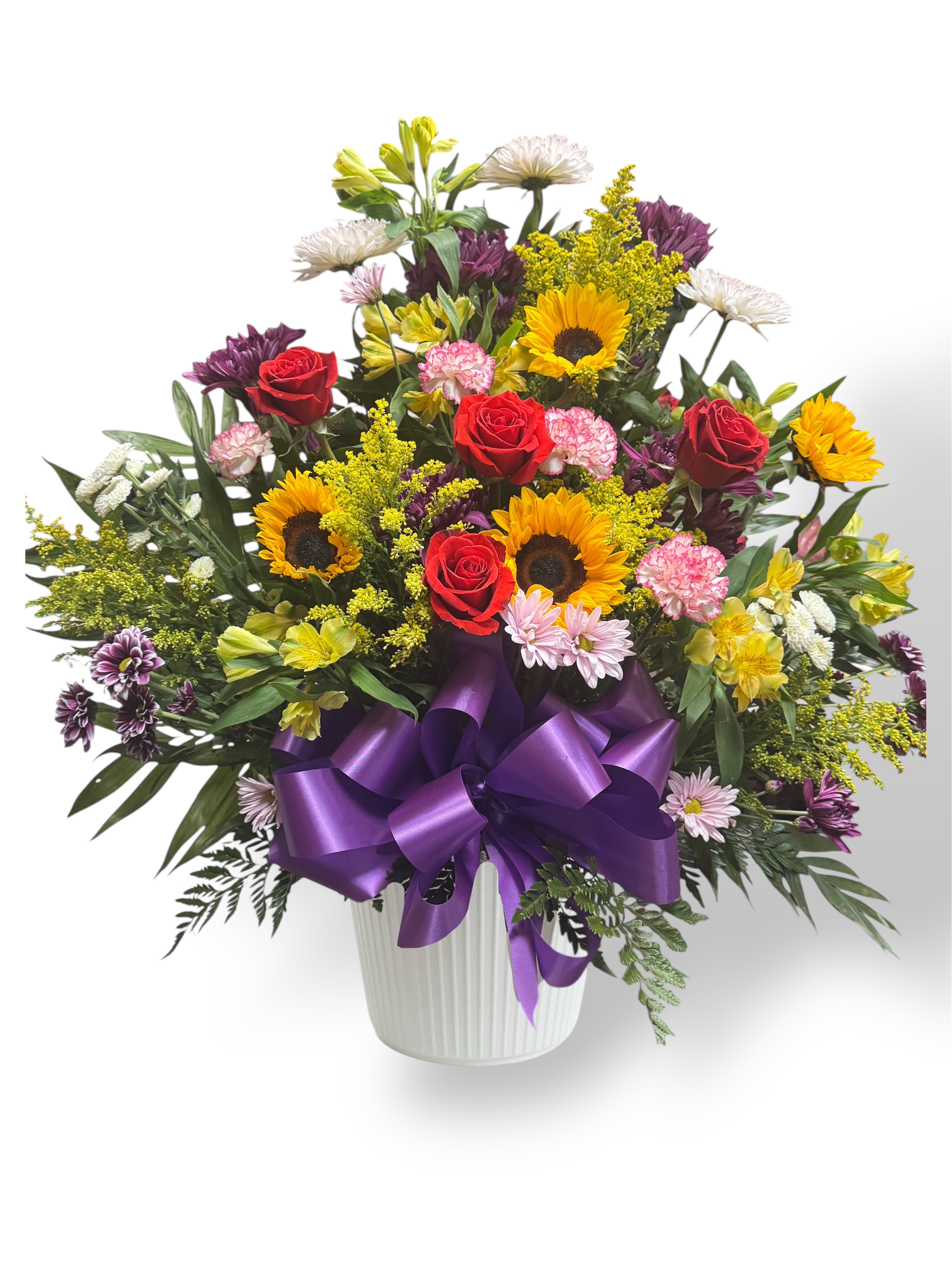 Mixed bouquet of roses, sunflowers, and daisies in a white vase with a purple bow