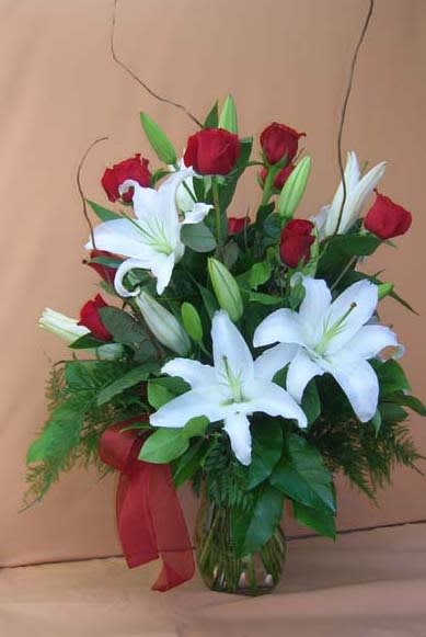 Red roses and white lilies in a glass vase with a red ribbon