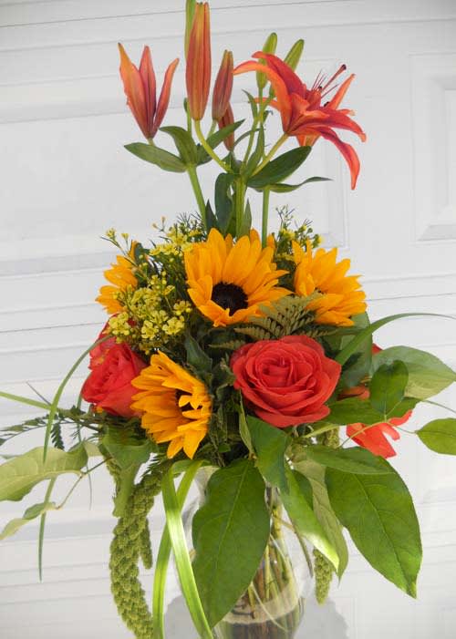 Bouquet of orange lilies, sunflowers, and red roses in a glass vase