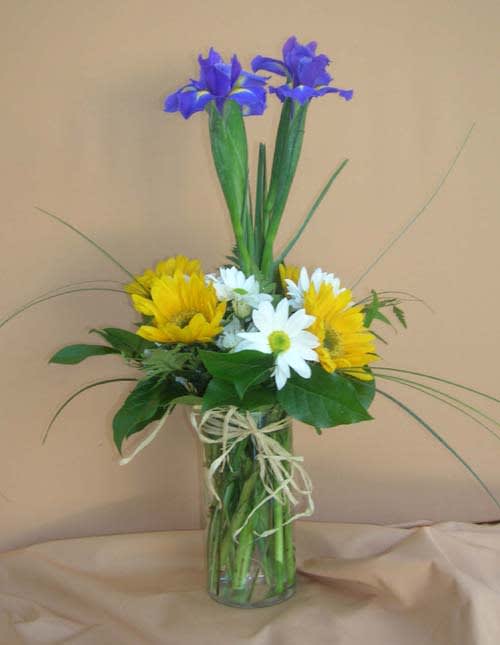 Yellow and white daisies with purple irises in a glass vase