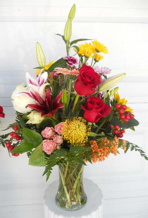Mixed bouquet of red roses, lilies, and yellow flowers in a glass vase