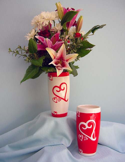 Pink lilies and white daisies in a tall heart-decorated vase with a matching cup