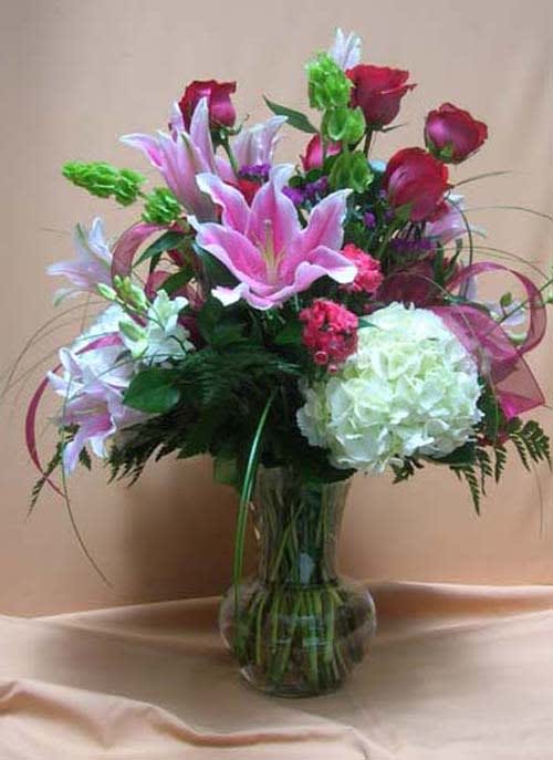 Pink lilies and red roses arranged in a clear glass vase